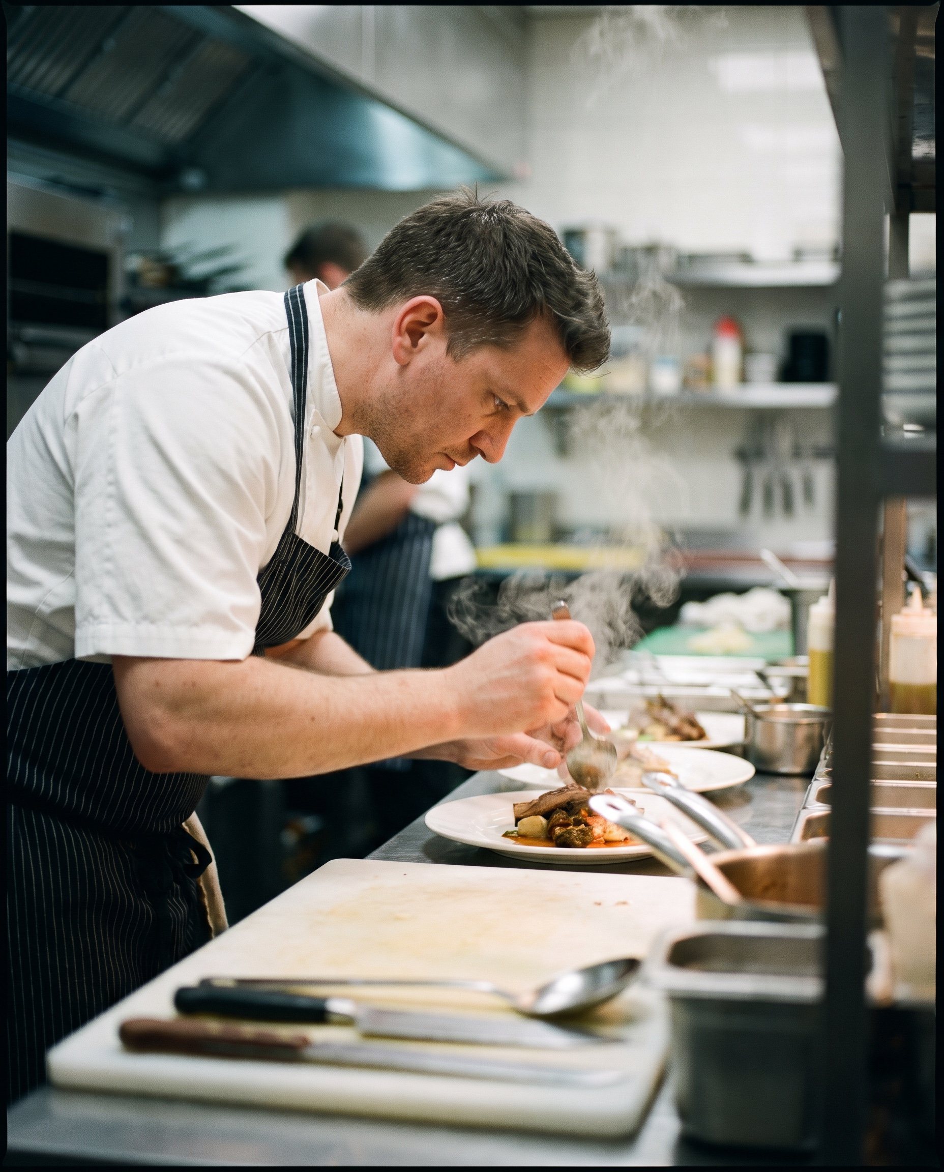 A chef working in a dim professional kitchen with steam rising, lit by warm overhead light