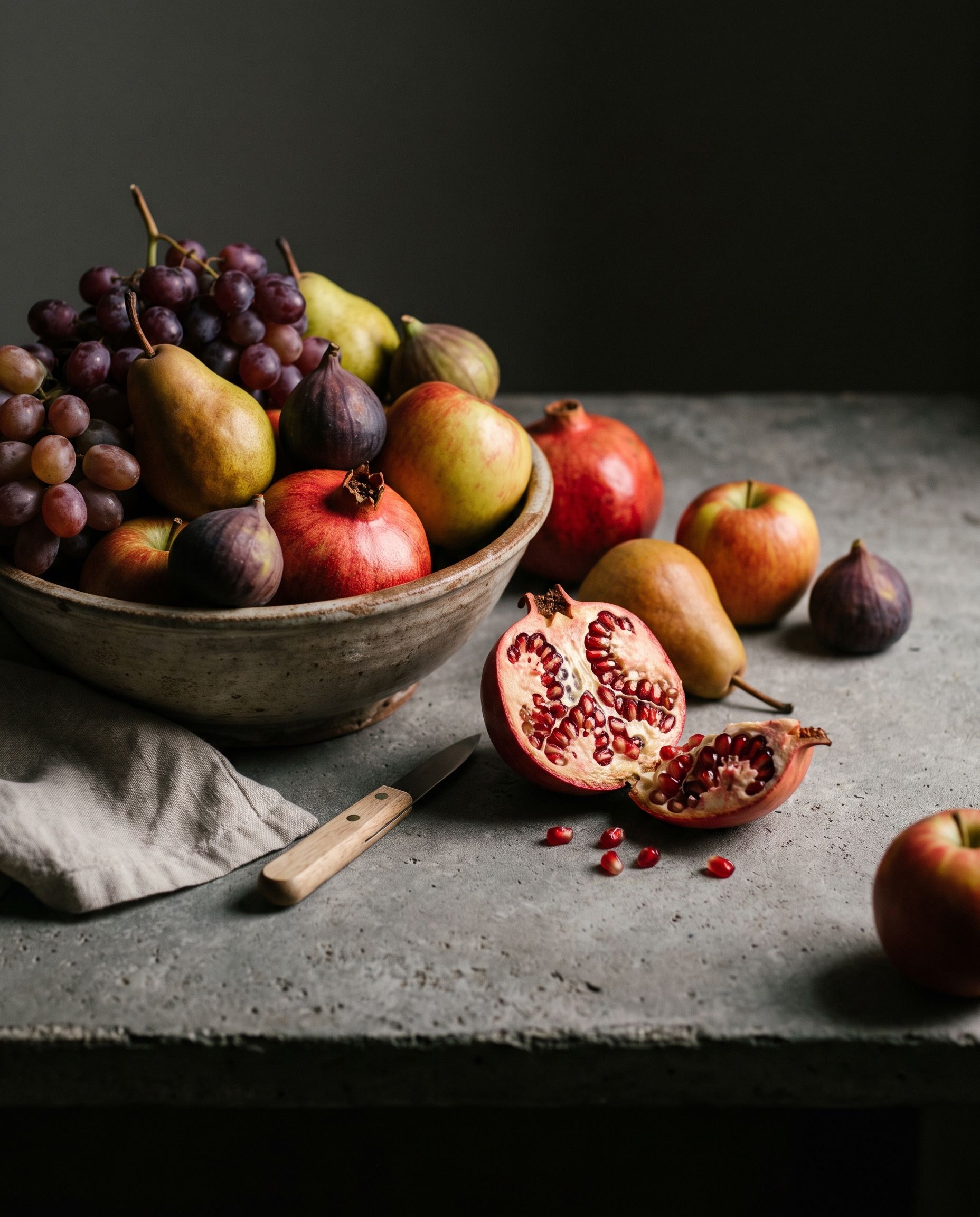 Ripe fruit and a rough ceramic bowl on dark linen, lit in deep chiaroscuro against a shadowed background
